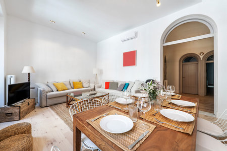 Nice living room with large sofas upholstered in gray fabric, wooden dining table with tableware set...
