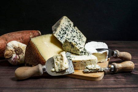 Still life with assortment of salty blue cheese, brie cheese, cured Spanish Manchego cheese, garlic...
