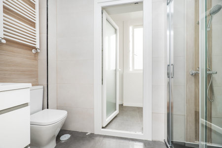 Tiled toilet with large white tiles, white porcelain sink, white aluminum towel radiator and shower...