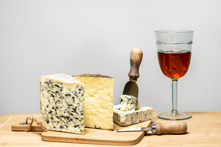 Delicious cheese wedges of different varieties with specialized cheese knives and a glass of Spanish wine on a cutting board eaten in turn on top of a bamboo tableの写真素材
