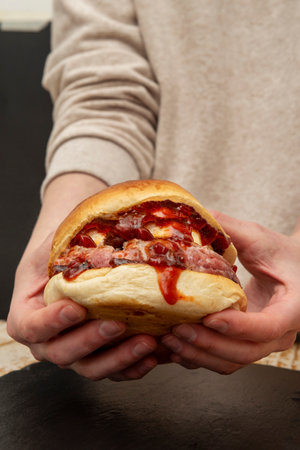 Delicious beef burger with goat cheese and lots of spicy tomato jam held in two handsの写真素材