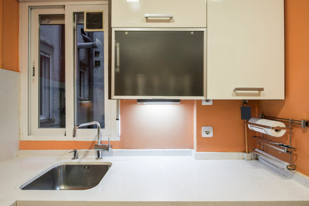 fitted kitchen with white cabinets with white marble countertops and orange painted walls and a stainless steel undermount sink with matching faucetの写真素材