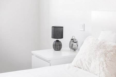 Headboard with white cushions, bedside table with lamp and chrome alarm clock
