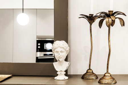 sideboard with a mirror leaning against the wall, classical roman bust and gold colored metal candle...