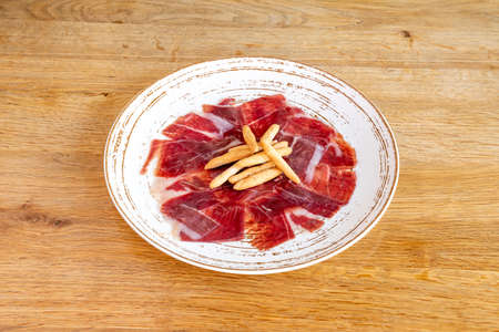 Acorn-fed ham tapas with croutons on a white plate on a wooden tableの写真素材