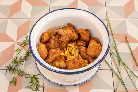 Fried chicken pieces with potatoes and rosemary in a deep enamel bowlの写真素材