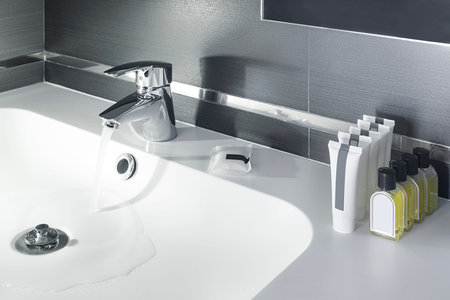White porcelain sink with chrome faucet that releases water and tidy amenities