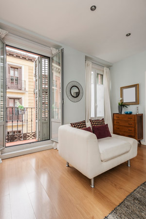 Vertical shot of a living room with a balcony with wooden shutters, a white corner sofa and a wooden sideboardのeditorial素材