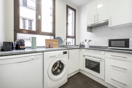 White kitchen with matching appliances, gray granite countertops and small countertop appliances, windows above the countertop and dark gray stoneware floorsのeditorial素材
