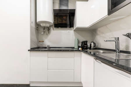 Corner of a kitchen with a black countertop and white cabinets with small appliances on the countertopのeditorial素材