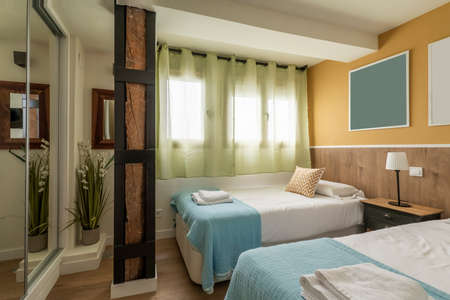 Bedroom with youthful beds with blue bedspreads, green net curtains and built-in wardrobe with sliding mirror doorsのeditorial素材