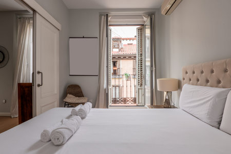 Bedroom with double bed, capitone upholstered fabric headboard, balcony with wooden shutters with...