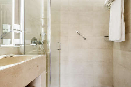 bathroom with cream colored marble sink, frameless mirror with integrated light and shower cabinのeditorial素材