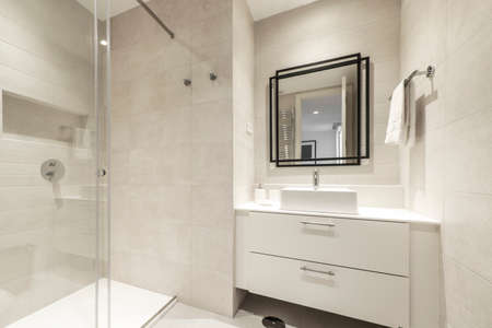 bathroom with white cabinets, shower stall with sliding glass screen, square wall mirror and cream tilingのeditorial素材