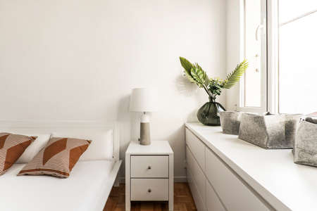 Corner of a bedroom furnished with white wooden furniture, decorative plants and cushions giving a touch of colorのeditorial素材