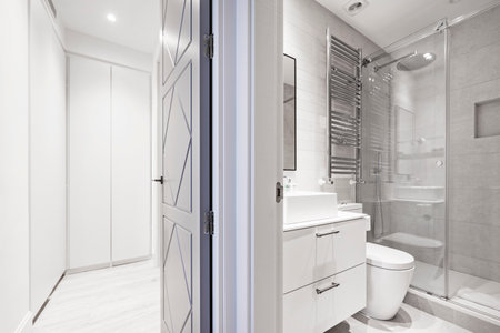 Bathroom with white resin sink, marble walls, white wooden furniture, shower cabin with screen, chrome towel dryer radiator and access to a dressing roomのeditorial素材
