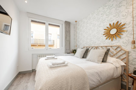 Bedroom with bamboo wood headboard, towels on the bed, sun mirror with gold frame, tv on the wall and white aluminum windowのeditorial素材