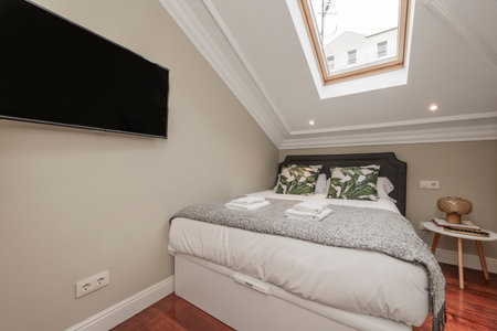 Bedroom with double bed with cushions and denim blankets, green cushions, skylight in the ceiling, tv hanging on the wall, white towels in the atticのeditorial素材