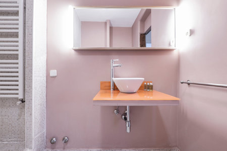 Bathroom with porcelain sink suspended over orange glass countertop, chrome tap, cabinet with mirror...