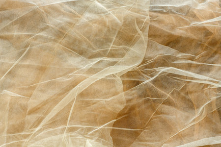 Subtle background of semi-sheer light cream colored tulle fabric with a visible pattern and some wrinklesの写真素材