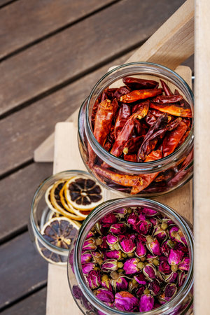 Top view image of a glass jar filled with dried tea roses and another with dried chili peppers on...