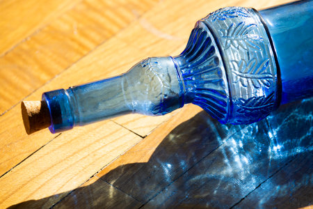 A blue decorative glass bottle on an oak surface pierced by a large ray of morning sunの写真素材