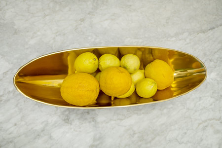 An elongated polished brass centerpiece filled with oranges and lemons on a polished white marble...