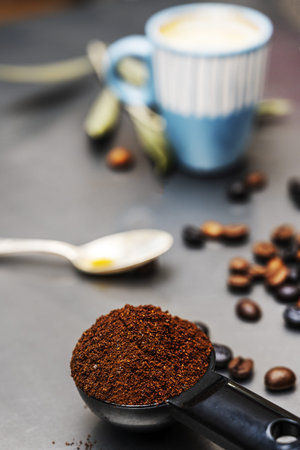Still life with ground coffee in the foreground with coffee beans behind and a cup in the backgroundの写真素材