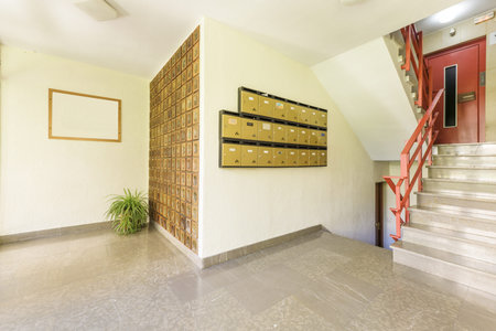 Portal of an old building with decorative indoor plants, elevator with red metal door, red railing...