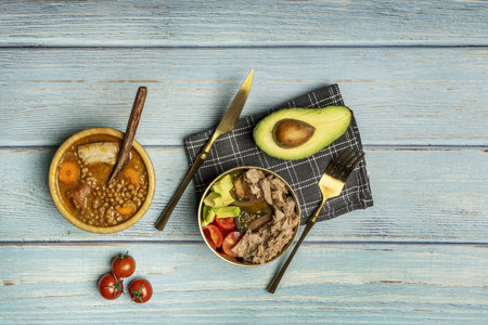An overhead still life of a menu with tomato and tuna salad for the first course and some stewed lentils on a light blue tableの写真素材