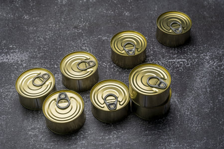 Some unopened circular cans of canned food with tabs for easy opening on a gray surface filled with...