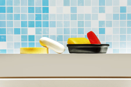 Black porcelain bowl with glycerin soap bars, a white soap bar and a yellow sponge on a white...