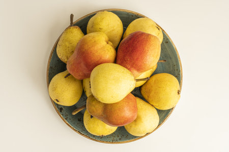 A plate overflowing with delicious ripe pears on a white shelf viewed from the topの写真素材