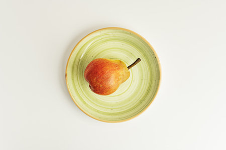 A single ripe lone pear on a green plate on a white shelf viewed from aboveの写真素材