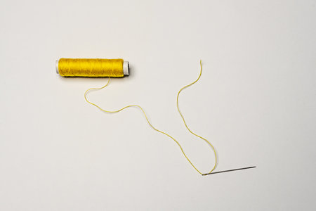 Spool of yellow thread with a needle threaded with thread on a white backgroundの写真素材