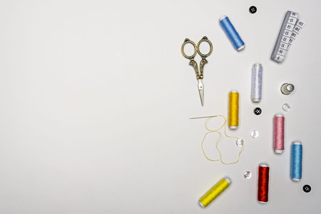 Set of spools of colored thread with a threaded needle, black and white buttons, golden scissors,...