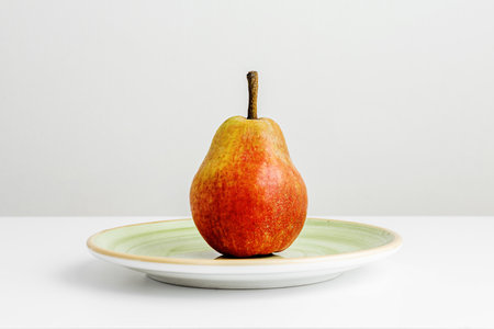A lone ripe pear on a green plate on a plain white surface and a white backgroundの写真素材