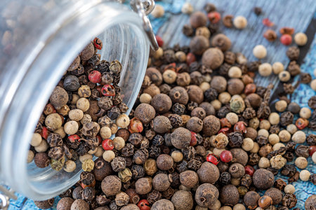 An upturned glass jar on a blue table full of piemoenta seeds of various kindsの写真素材