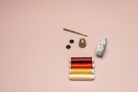 A copper thimble, a tape measure, spools of thread and a light pink backgroundの写真素材