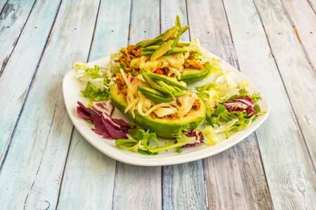 Avocado salad stuffed with shredded meat and fresh cheese on a white plateの写真素材