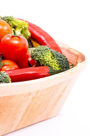 A light wooden basket filled with ripe cherry tomatoes, broccoli chunks and red hot chili pepersの写真素材