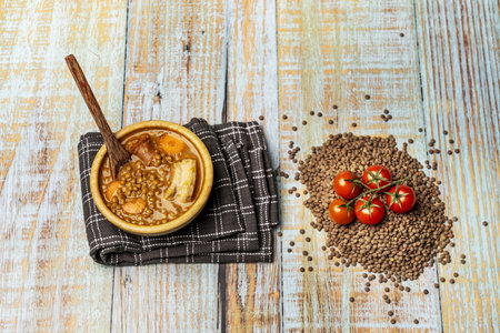 Still life with traditional lentil stew in a wooden bowl on a light wooden table with dried lentils and strings of cherry tomatoesの写真素材