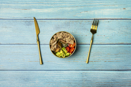 A still life with salad with various types of diced tomato, avocado and a lot of canned tuna with golden cutlery on a blue tableの写真素材