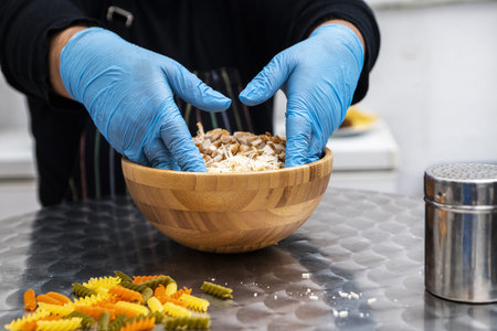 Gloved hands of a chef mixing a chicken and cheese salad in a wooden bamboo bowlの写真素材
