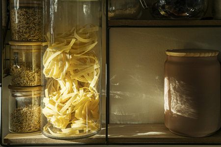 A shelf full of jars with cooking ingredients and nests egg pasta in a glass containerの写真素材