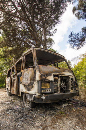 Abandoned burning van next to a forest totally wreckedの写真素材