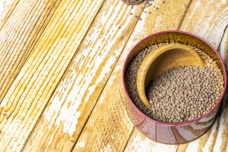 Dried lentils in a red metal bowl on a yellow planked tableの写真素材