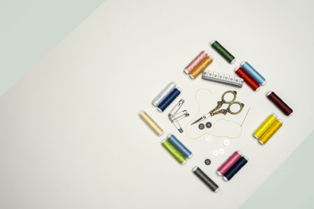 still life with a square formed by spools of thread of various colors, vintage-style metal scissors, white tape measure and black and white buttonsの写真素材