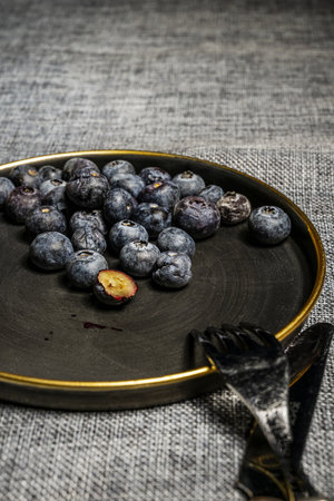 Image with focus on the well-ripe blueberries that are inside a black plate with a golden rimの写真素材