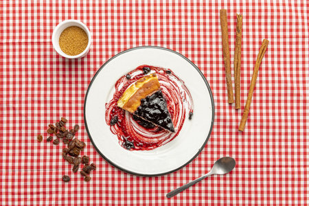 Top view of cheesecake with blueberry jam on an enameled plate, raisins, cinnamon stick and brown sugarの写真素材